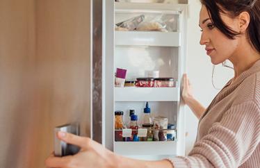 A woman stands in her kitchen opening her fridge to investigate potential sources for weird smells in the house.