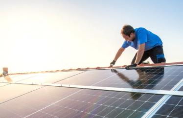 A man works on a solar panel on the roof of a home