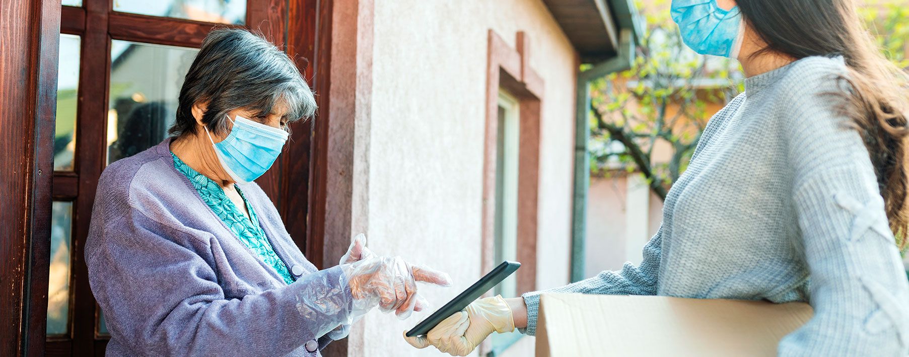 A woman in a mask delivering a package to a senior in a mask.