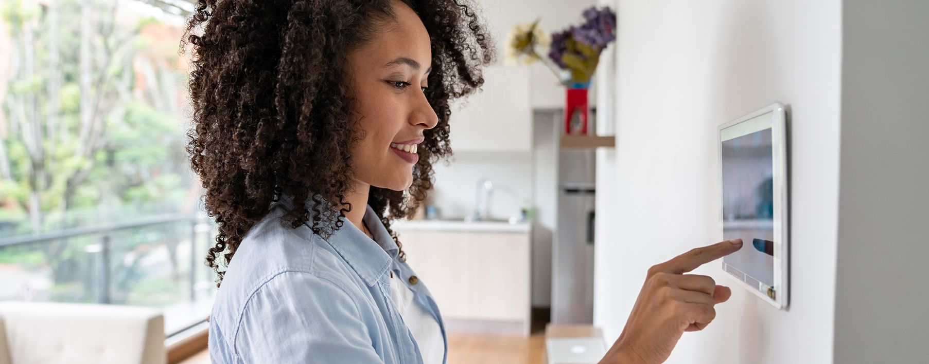 Woman using a smart home thermostat on a wall in her home.