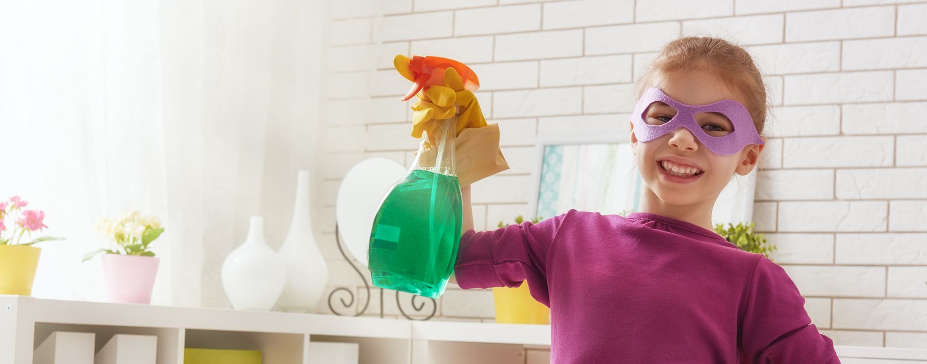 Young girl wearing a superhero mask holds a spray bottle.