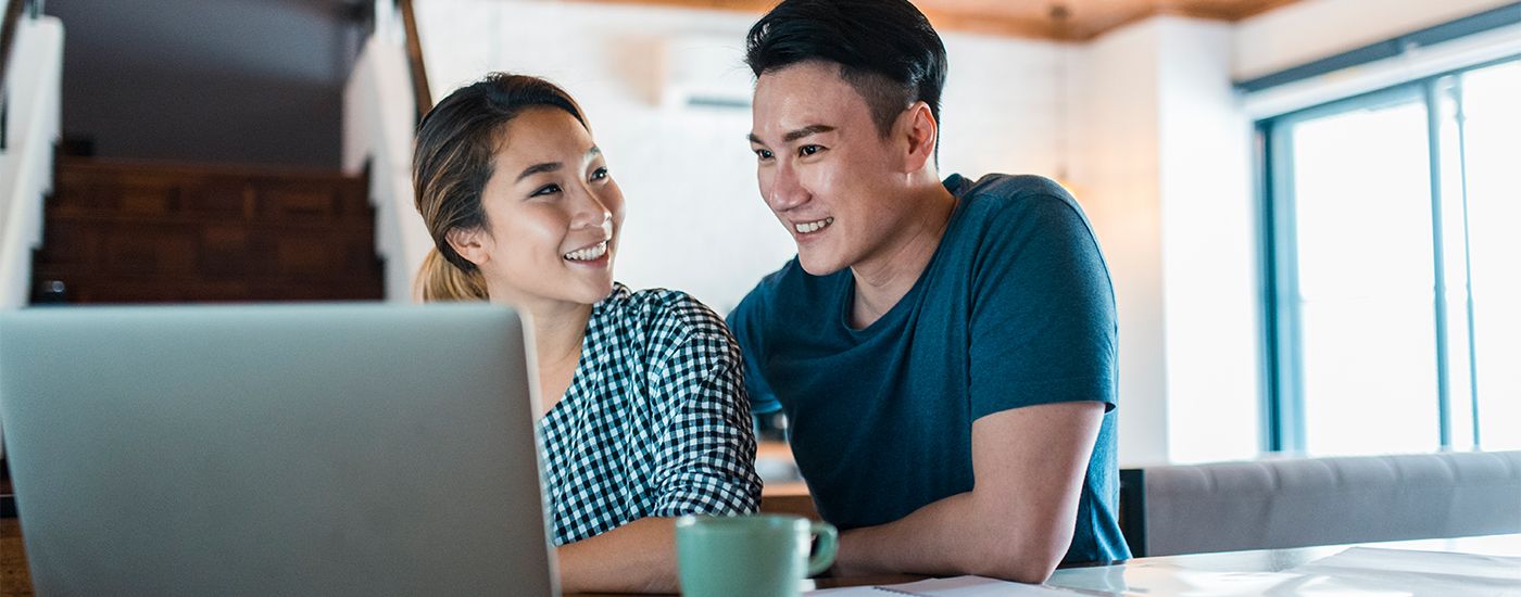 A young couple smiling at each other in front of a laptop