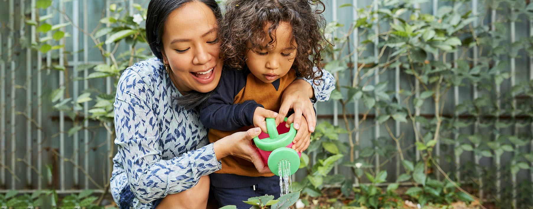A woman and a young boy watering a plant with a toy watering can