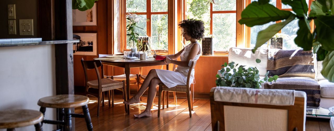 A woman writing at a desk by a window with plants around her