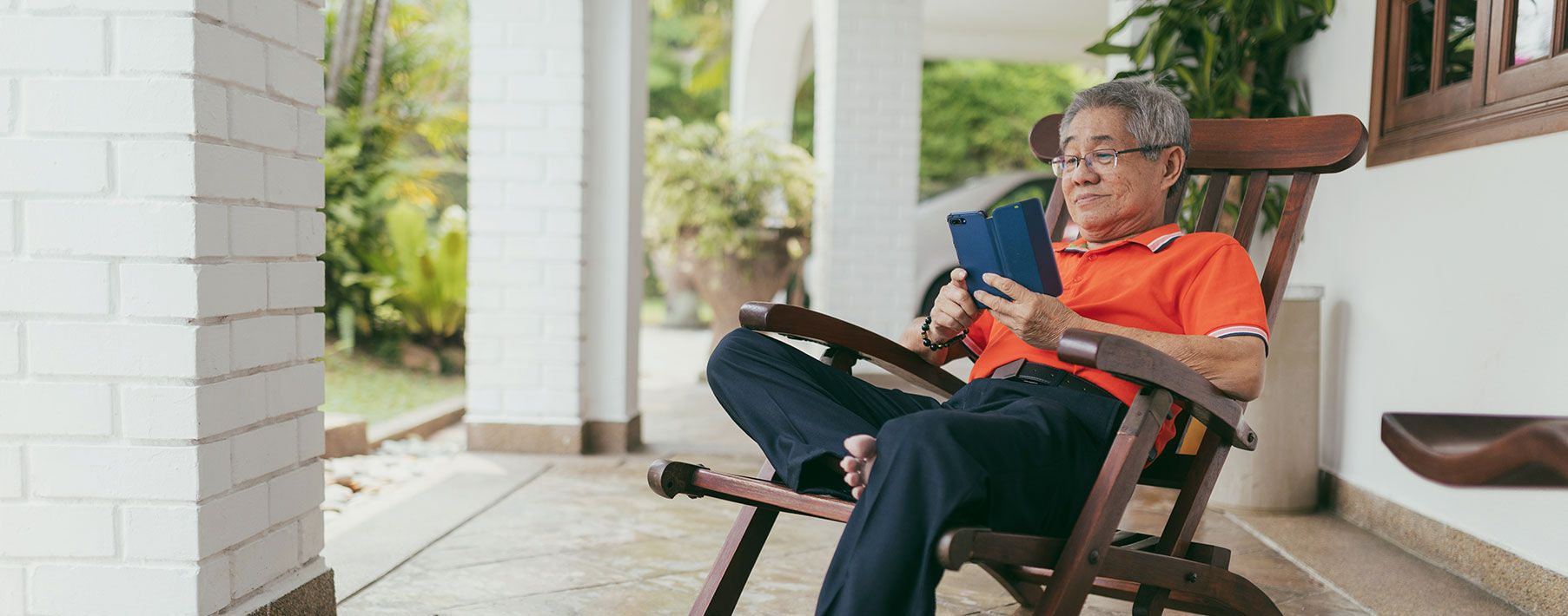 An older man reading his phone on a rocking chair on a front porch