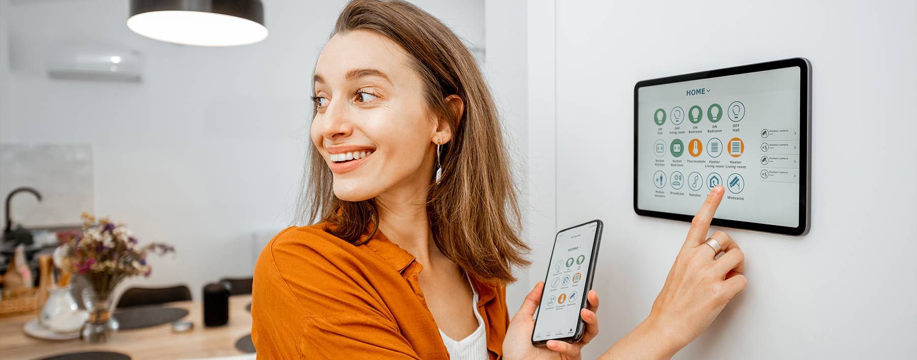 A woman smiling while using a tablet in the wall and holding a smart phone