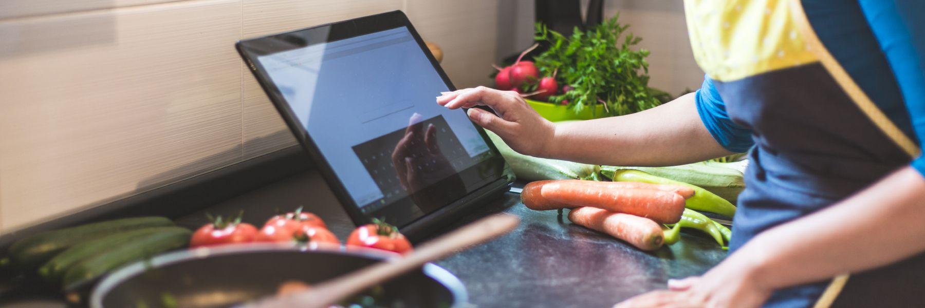 A person using a tablet in the kitchen with vegetables nearby