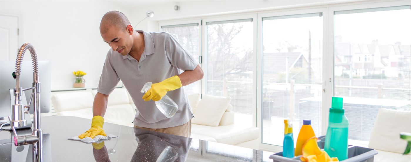 A man cleaning a kitchen counter with a cloth wearing yellow gloves