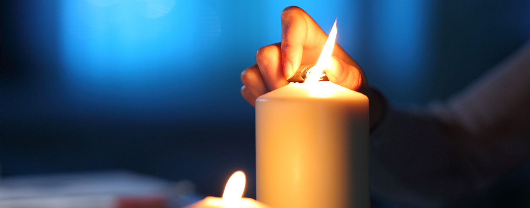 A close up image of a person's hand using a lighter to light a candle in the dark