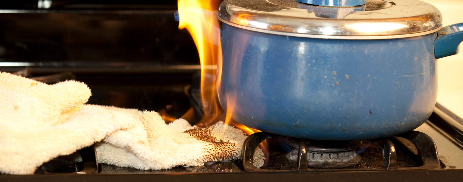 A rag sits on a stovetop under a blue ceramic pot. The rag is on fire. 