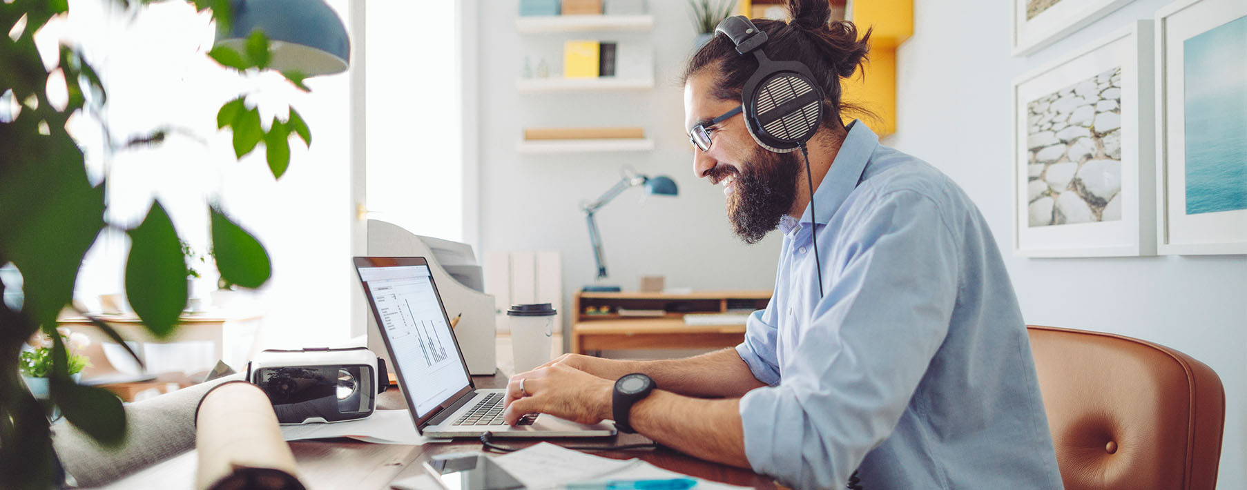 A man works on a laptop at a desk with headphones on