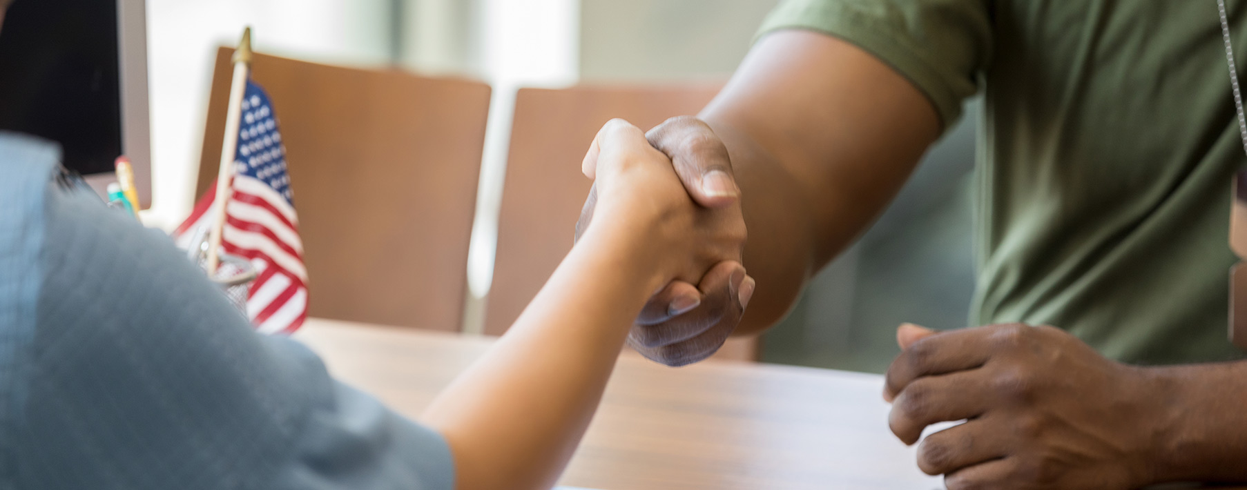 Two people shake hands over a table. Both are only visible from the shoulders down. 