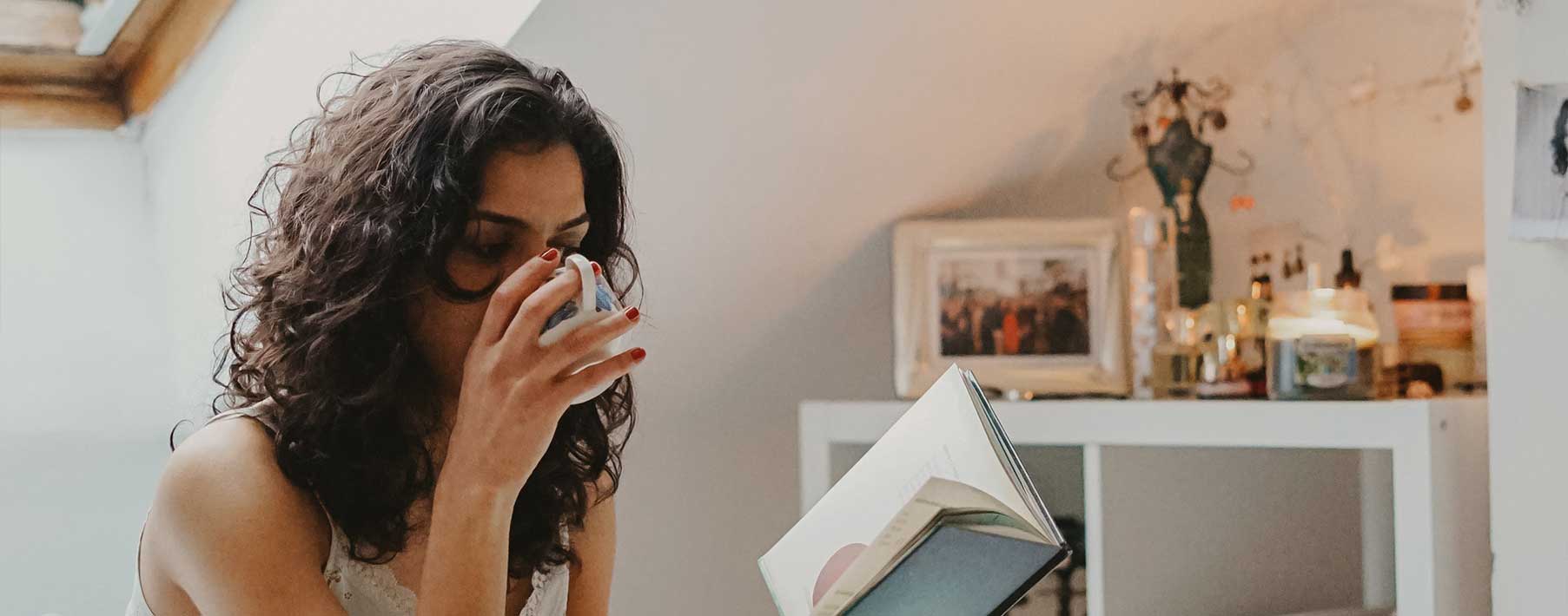Image of a woman drinking from a mug and reading a book