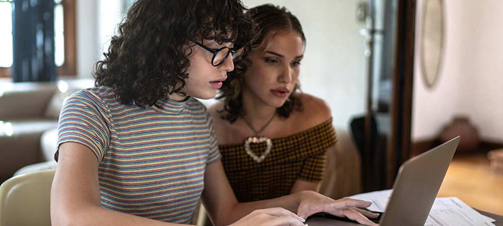 Two people looking at a computer with paperwork on the side. 