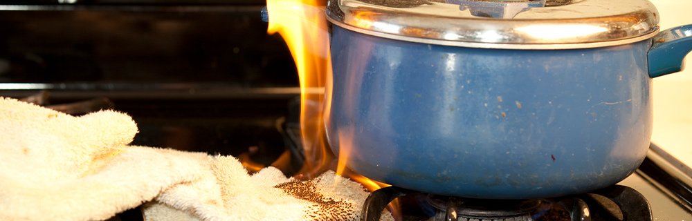 A rag sits on a stovetop under a blue ceramic pot. The rag is on fire.