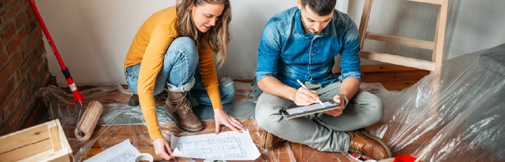 couple looking at plans on the floor of their home and preparing for home upgrades