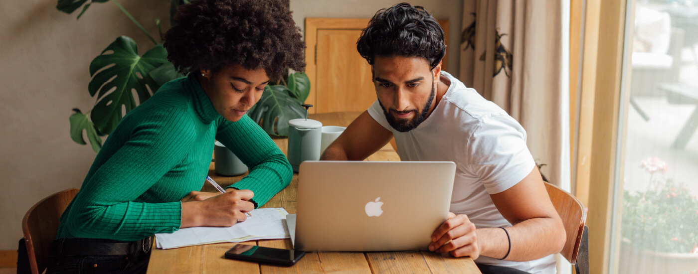 homeowners looking at a laptop and writing down notes to prepare for hail season