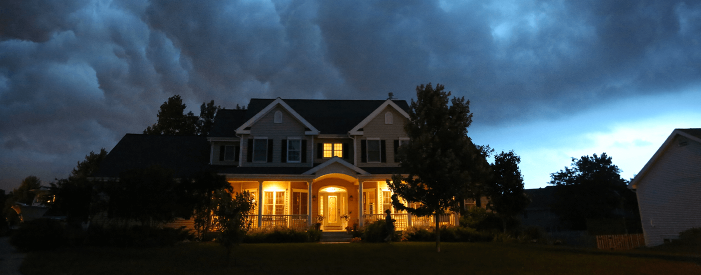home in the evening with lights on and stormy clouds hovering above it
