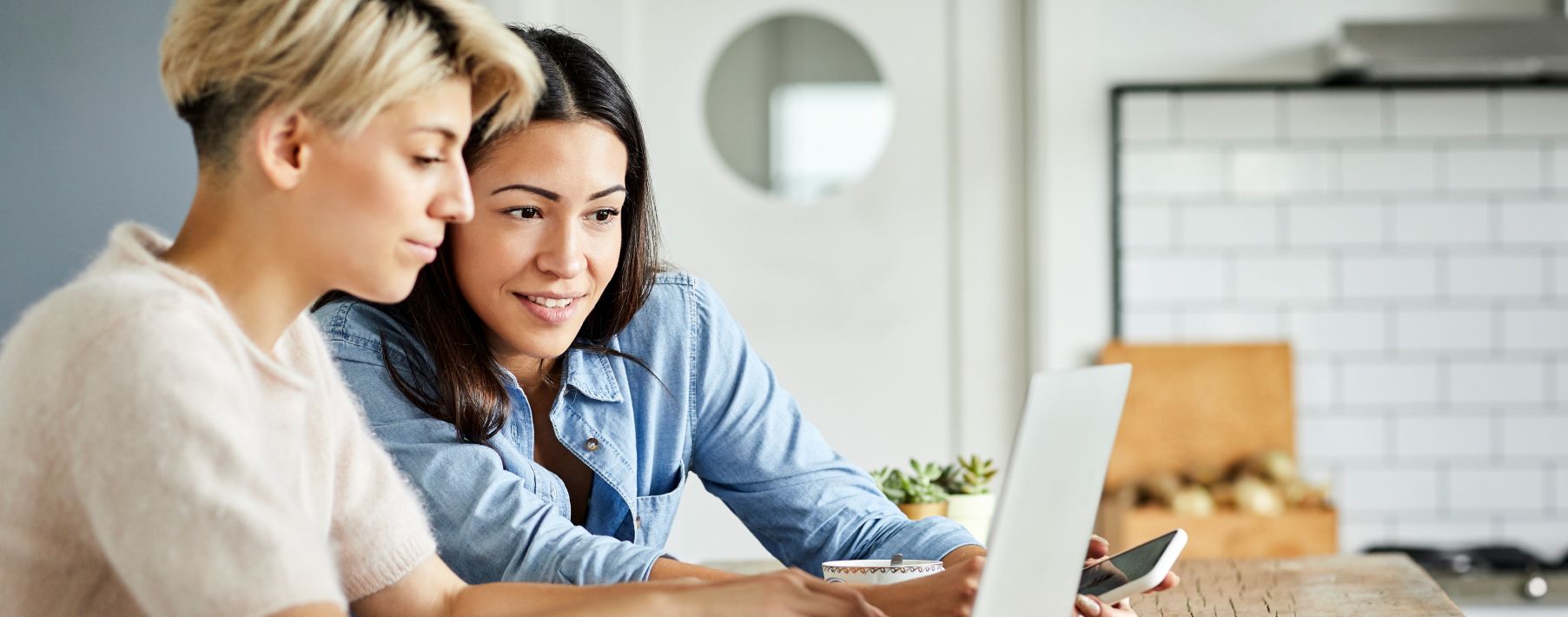 Two people sit at a desk looking at a laptop, one is smiling.