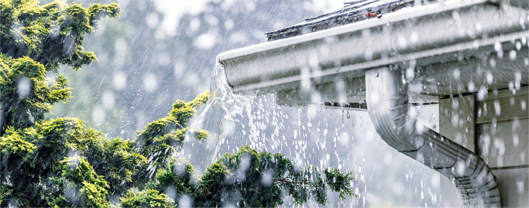 Image of the corner of a roof of a house during a rainstorm with water splashing out of a gutter