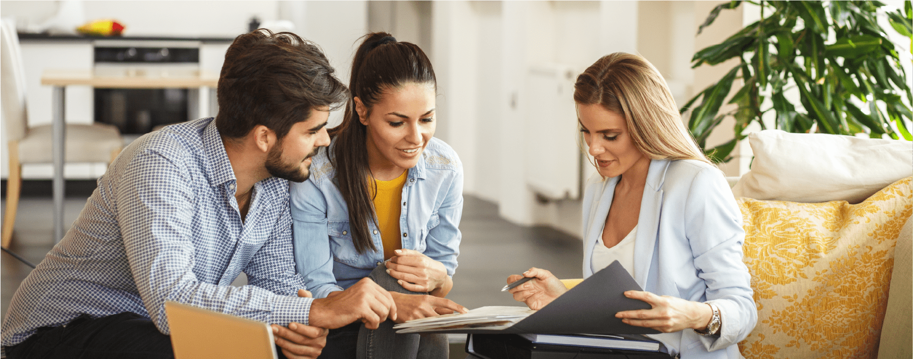 A man and a women sitting on a couch in an office, looking at paperwork with another woman