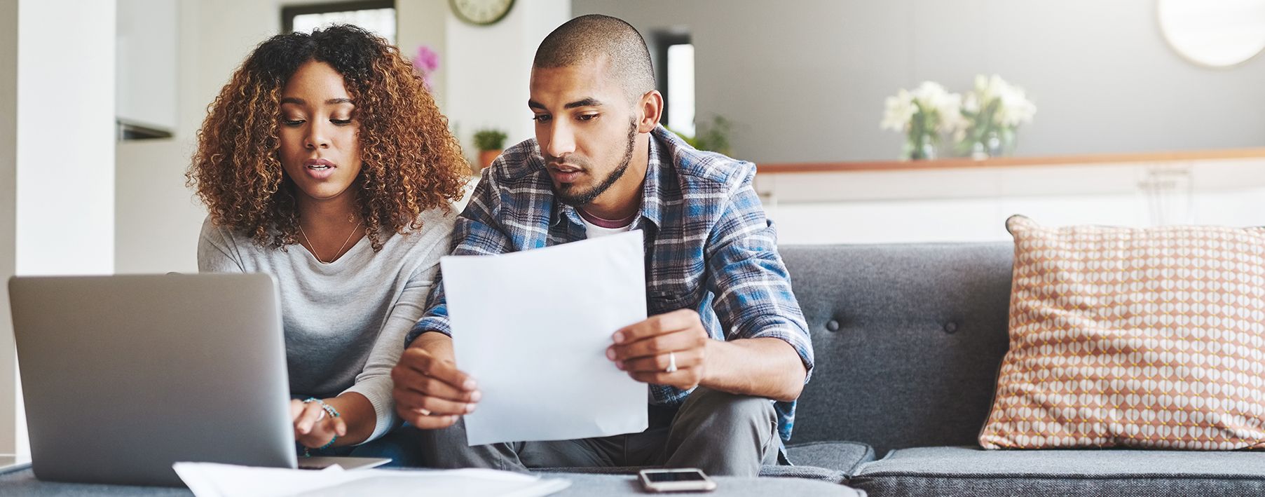 alt="A couple sitting on a couch looking at a laptop and papers"