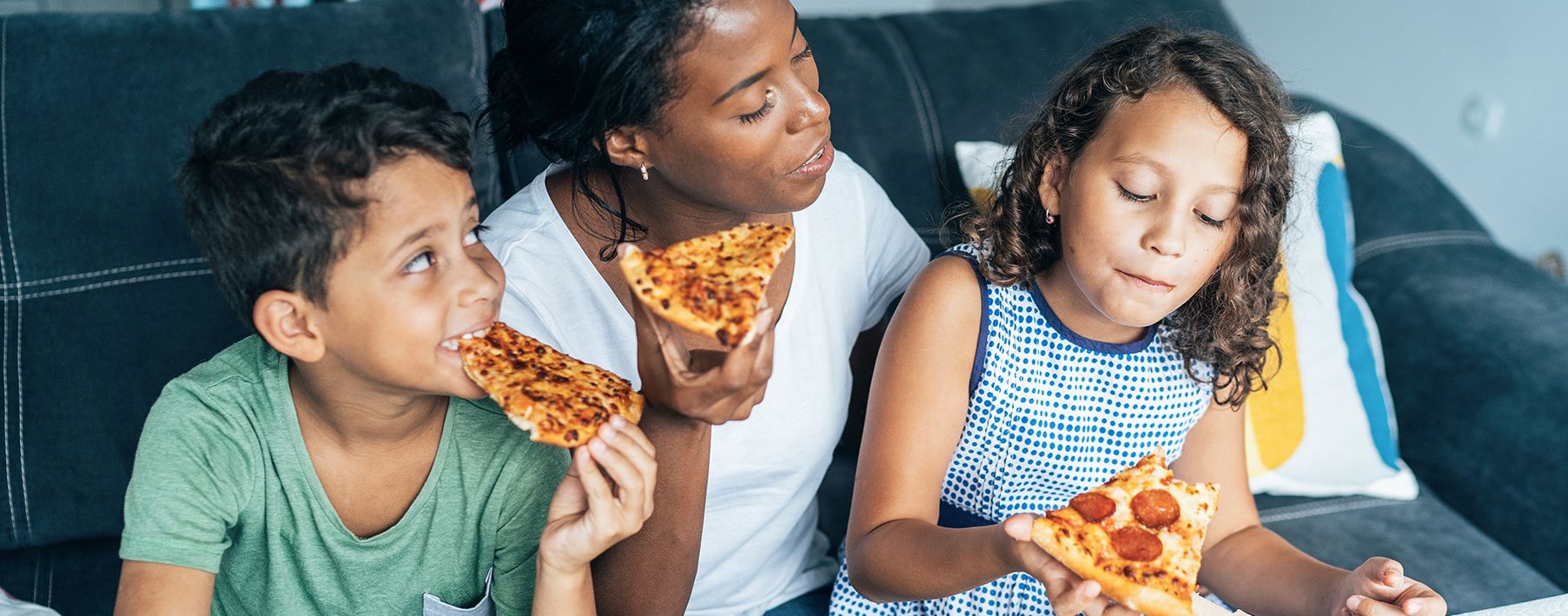 A mother and her two kids eating pizza on a couch