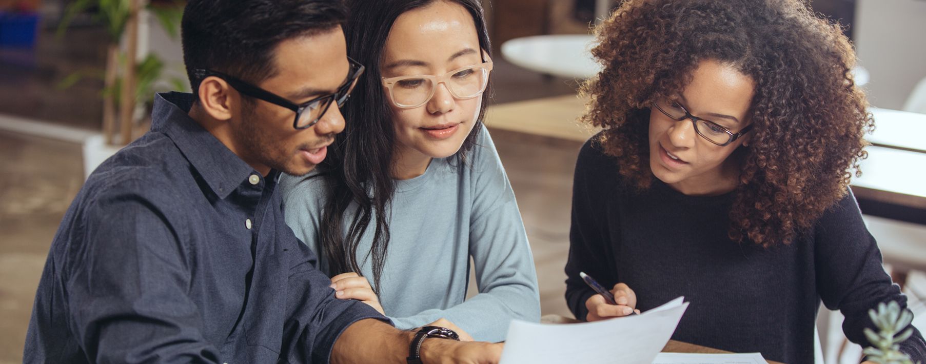 A man and woman looking at a piece of paper with another woman showing them something