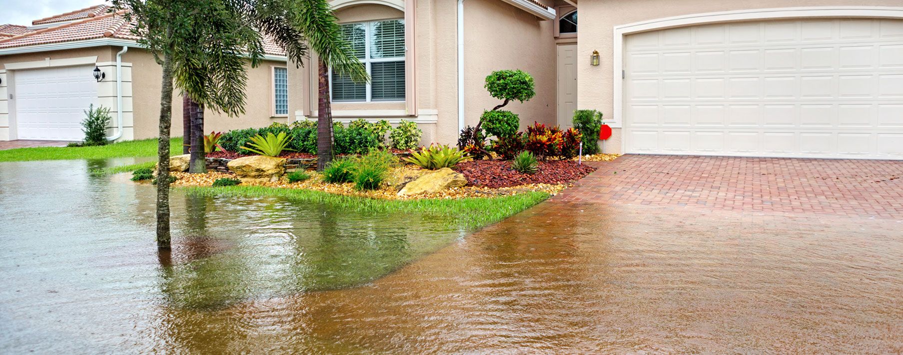 Image of water coming up a driveway in from of a light tan house