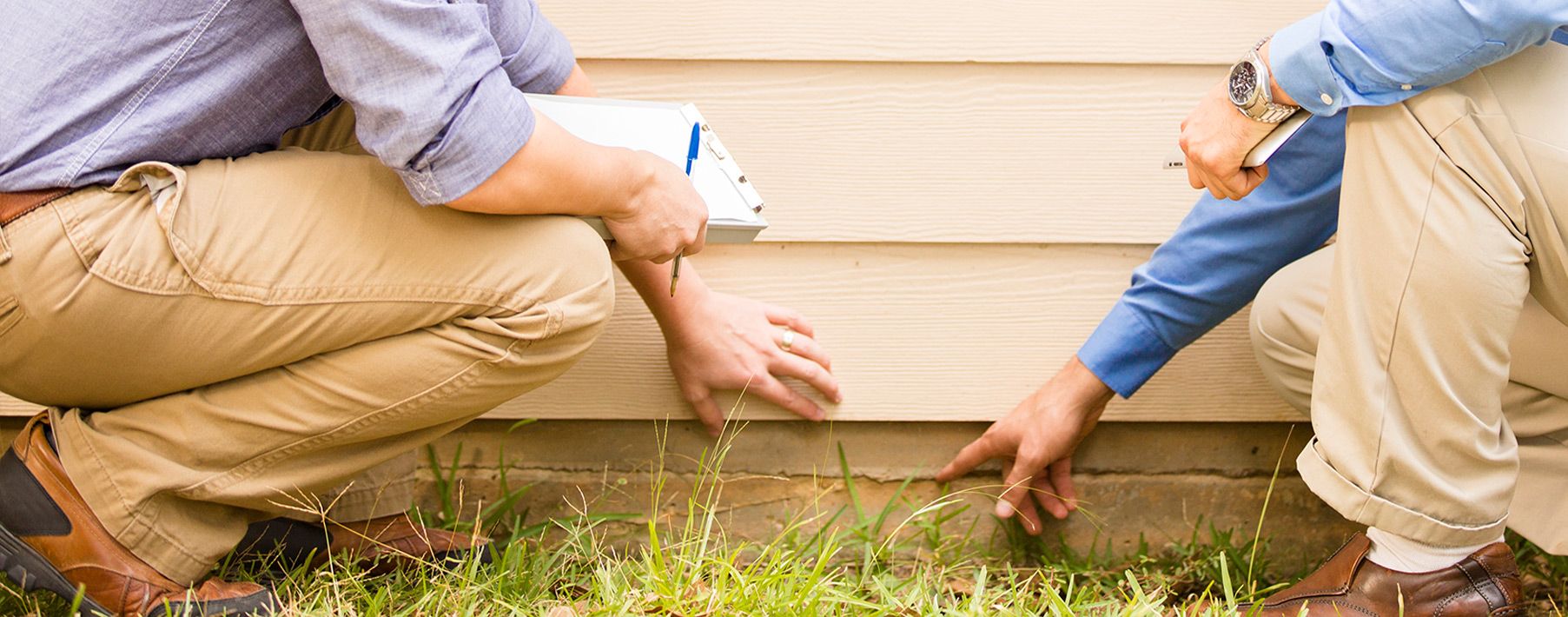 Two people squatting by a house pointing at a crack in the foundation