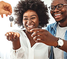 A couple laughing a reaching for a persons hand that is handing them keys