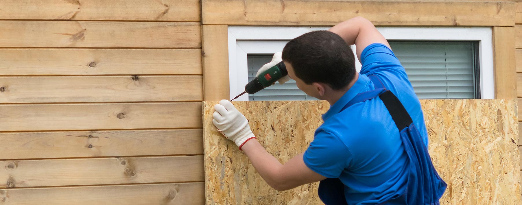 man drilling plywood over window