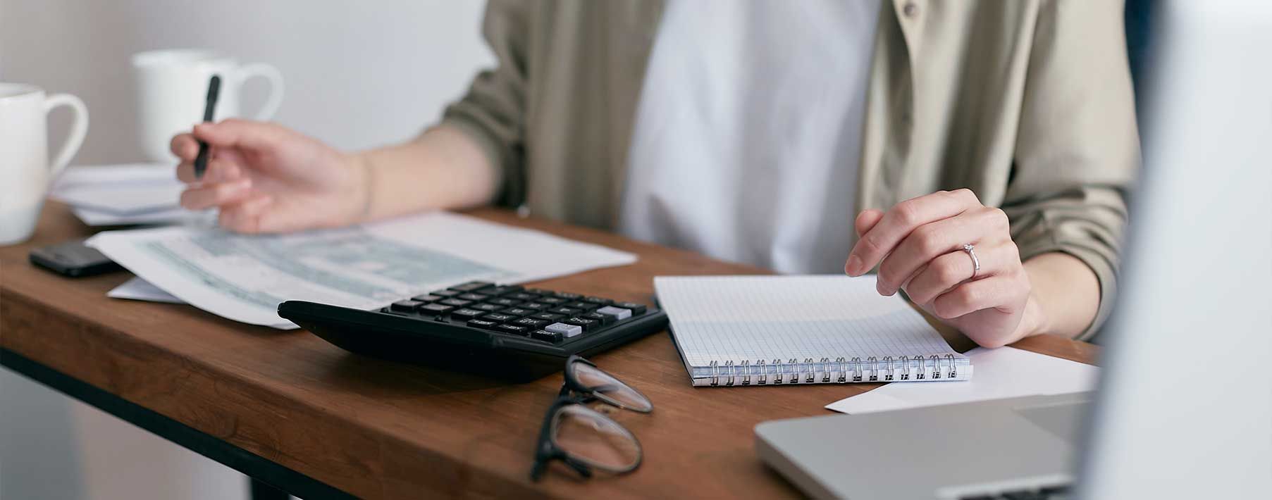 Image of a woman's torso and hands writing on a notebook and using a calculator