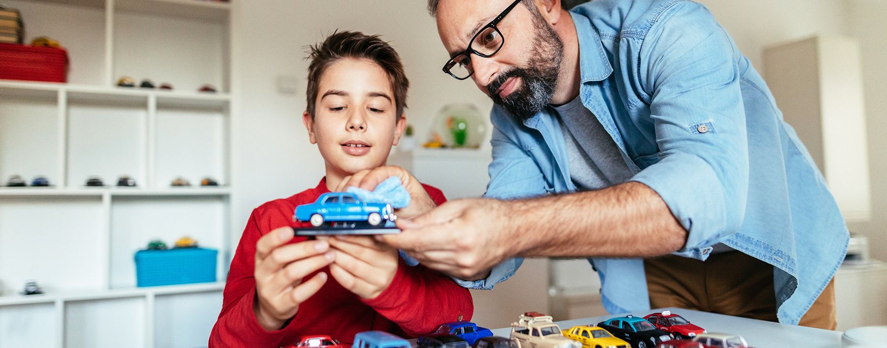 A father and son playing with a toy car in a kids room