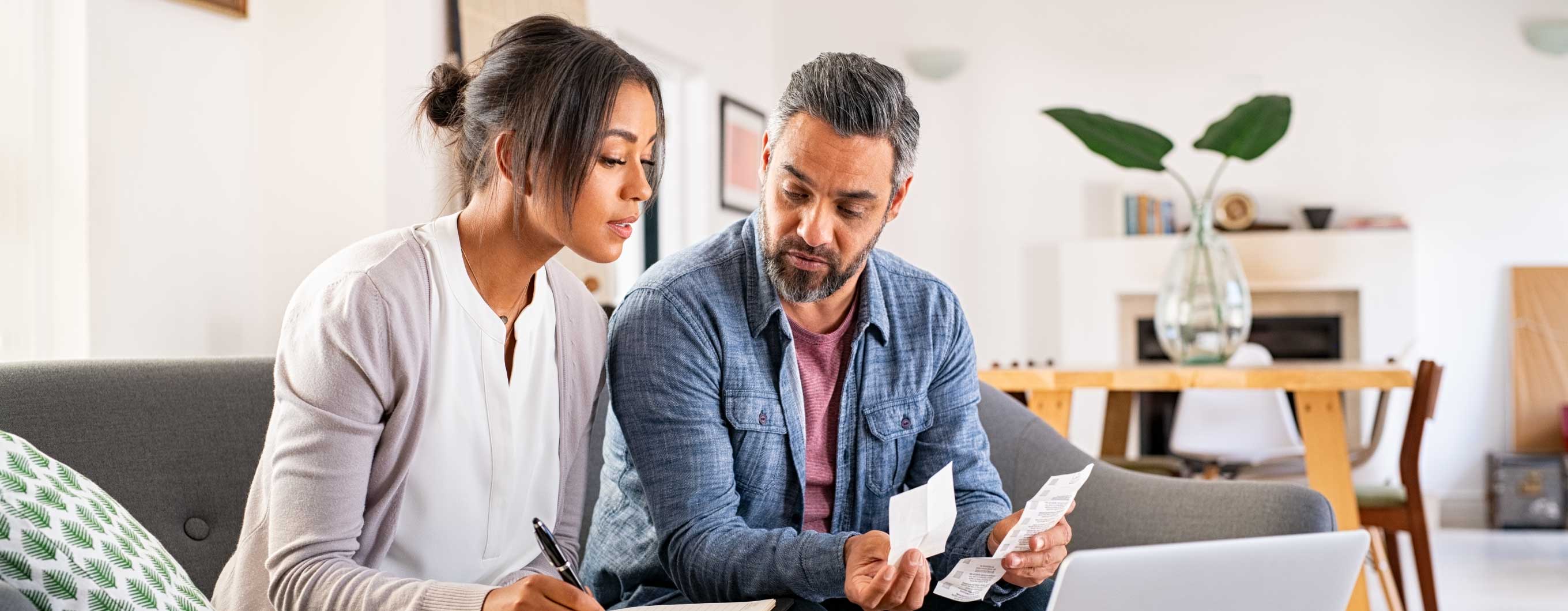 A man and a woman looking at receipts on a couch