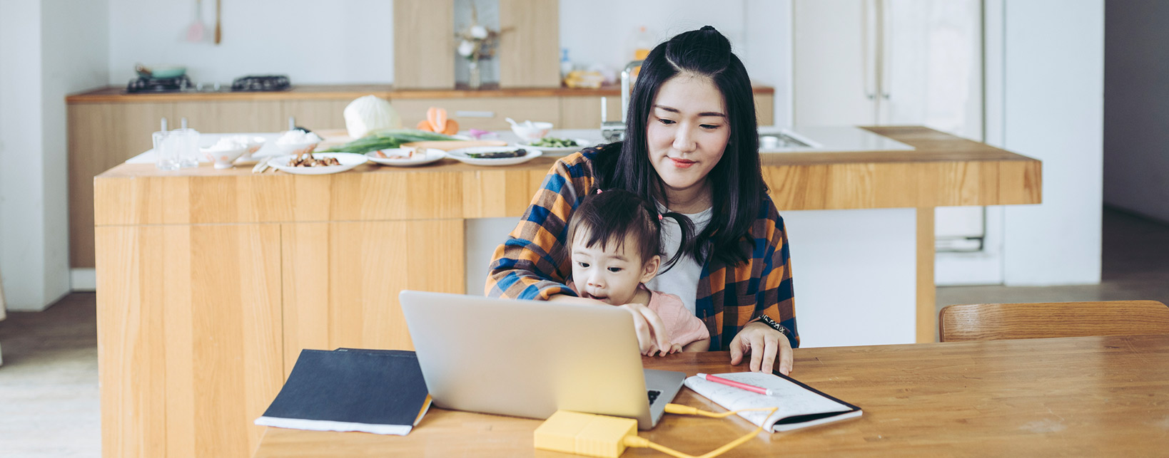 A mom holding child while sitting in front of a laptop