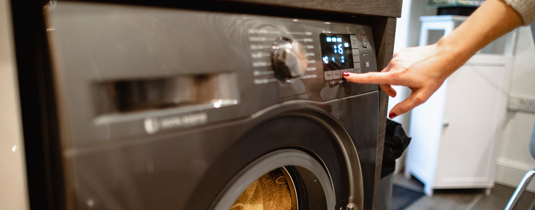 A woman's hand touching buttons on a washing machine
