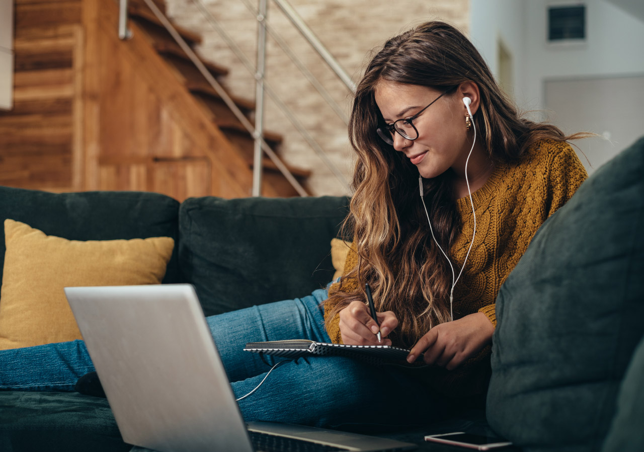 woman taking notes while watching a laptop