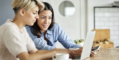 Two people sit looking at a laptop, one is smiling