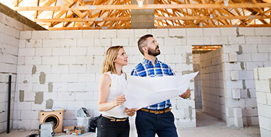 A man and a woman holding a blueprint inside a home under construction