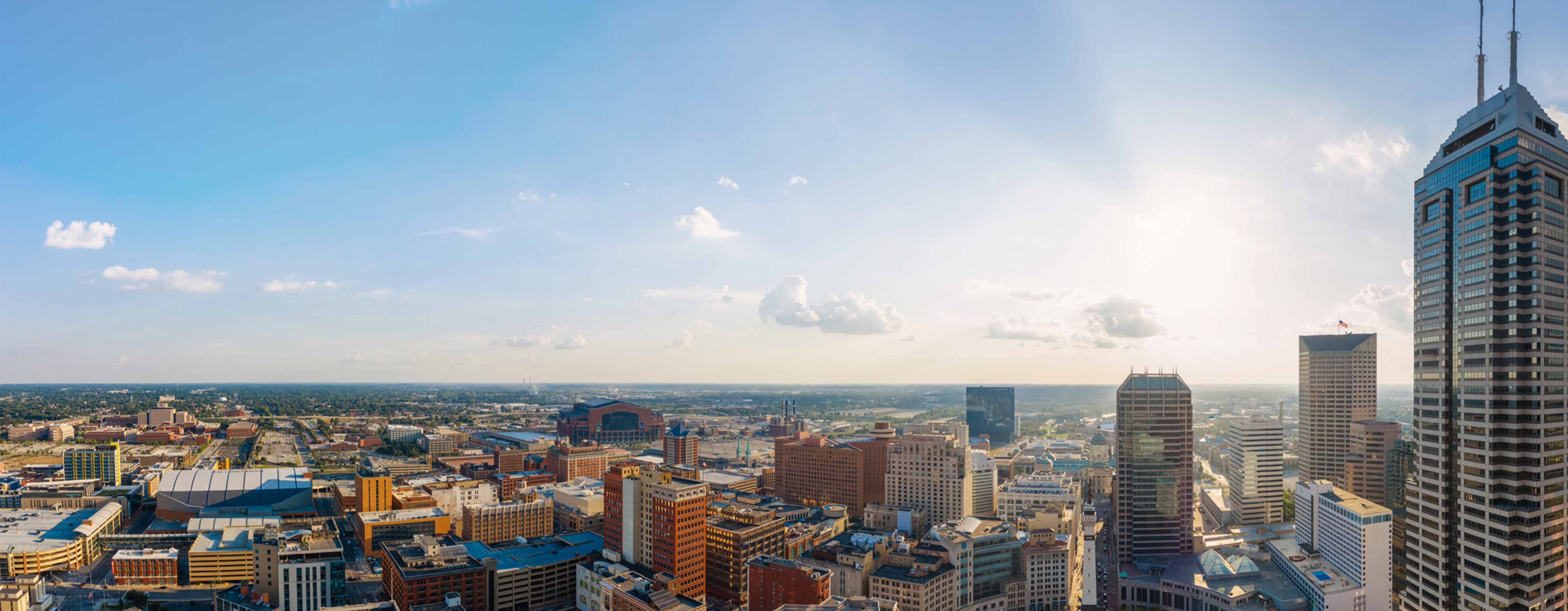 Image of Indianapolis, Indiana on a bright and sunny day. There are a few clouds in the sky. Skyscrapers are visible.