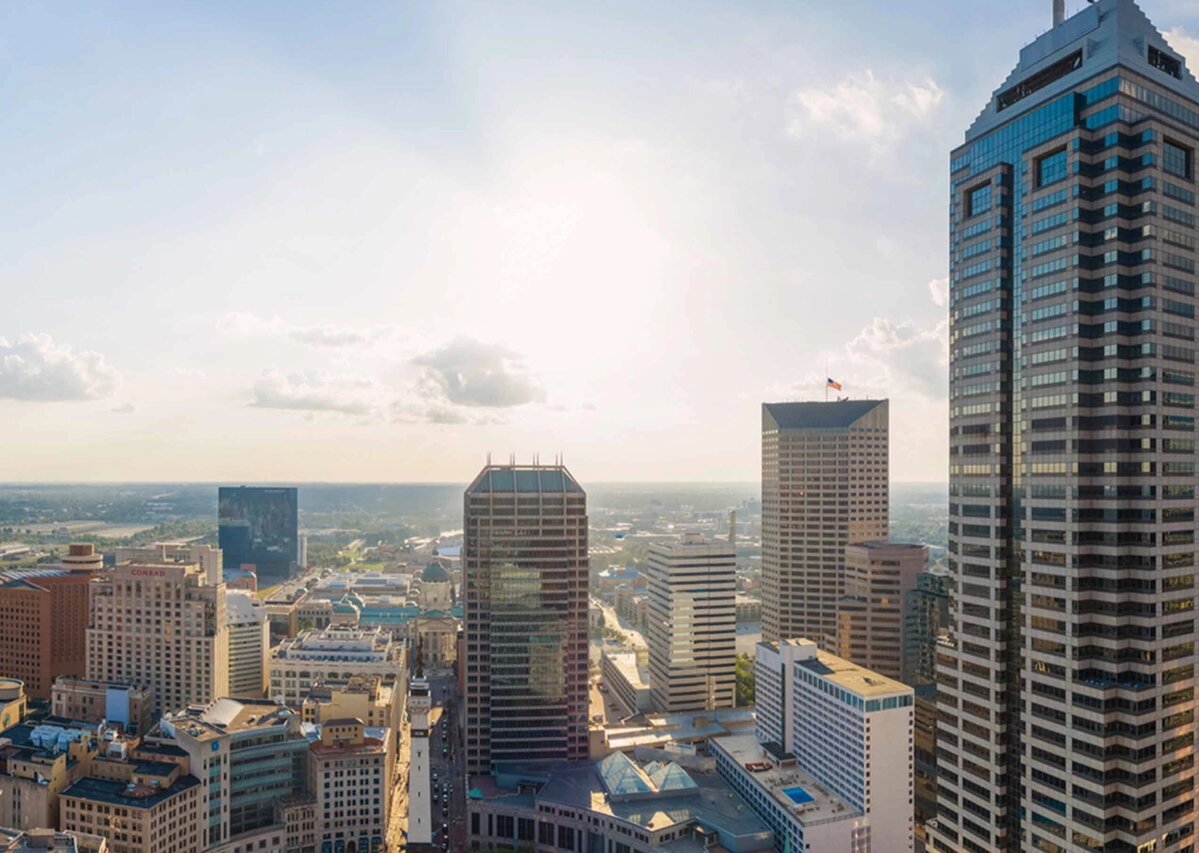 Image of Indianapolis, Indiana on a bright and sunny day. There are a few clouds in the sky. Skyscrapers are visible.