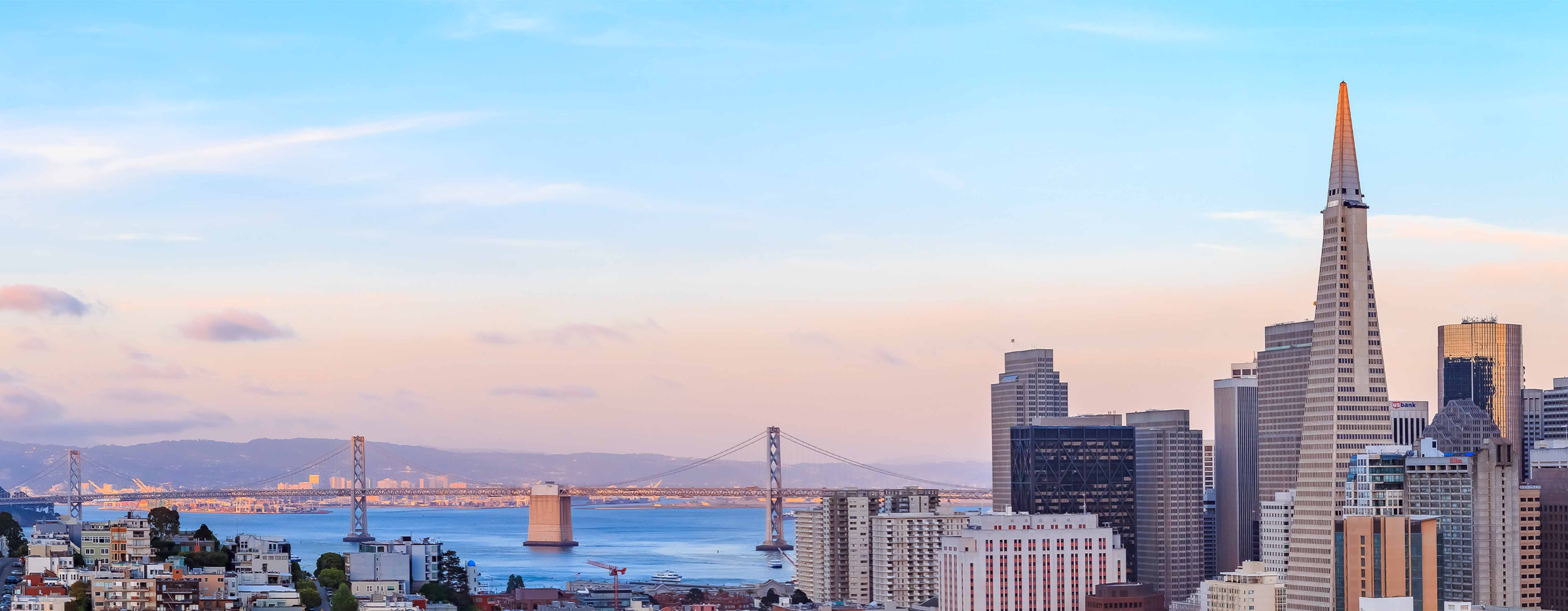 Image of the San Francisco city skyline with a body of water and golden gate bridge in the background