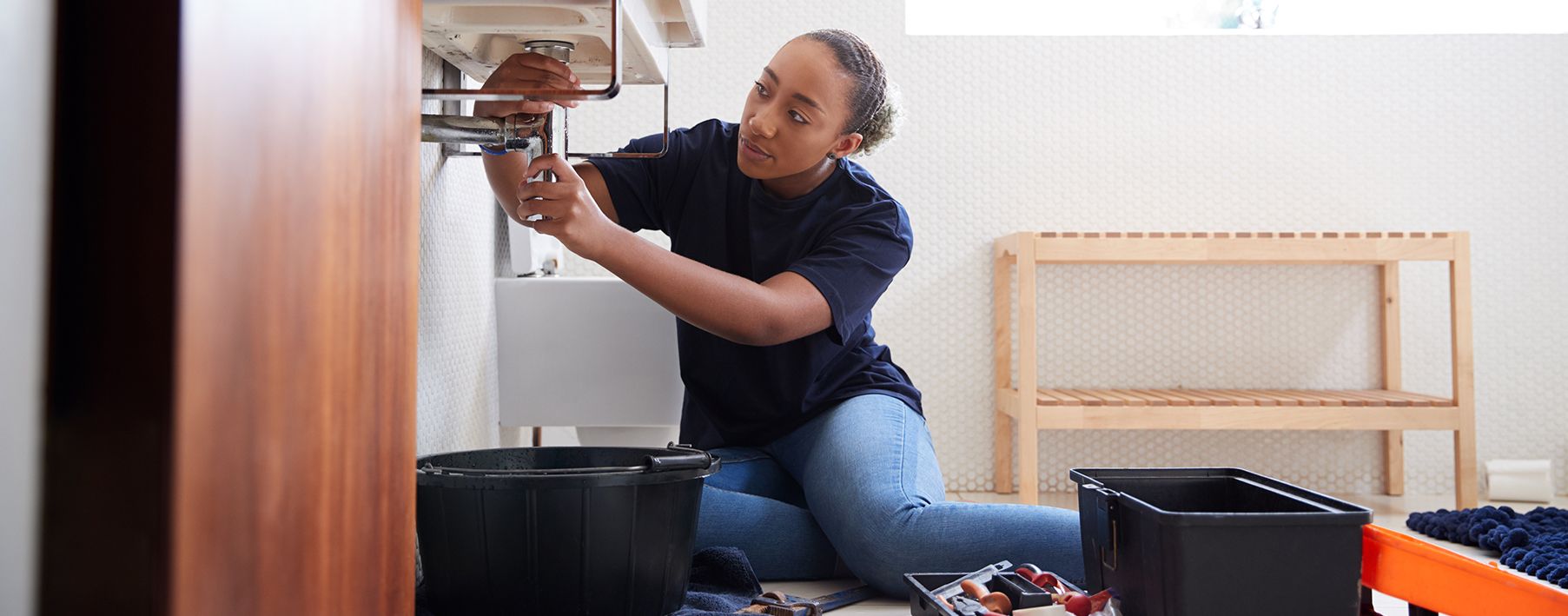 A woman sitting on the floor of the bathroom working on the sink