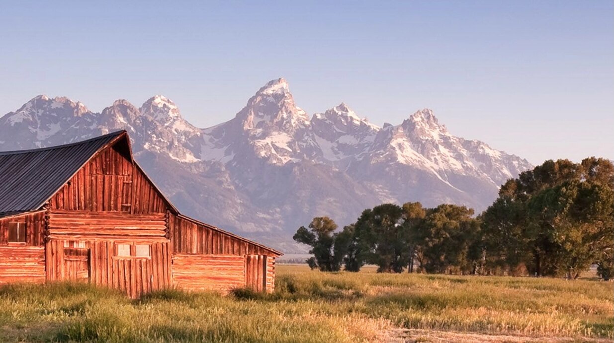 Image of red barn in a field with trees and mountains in the background