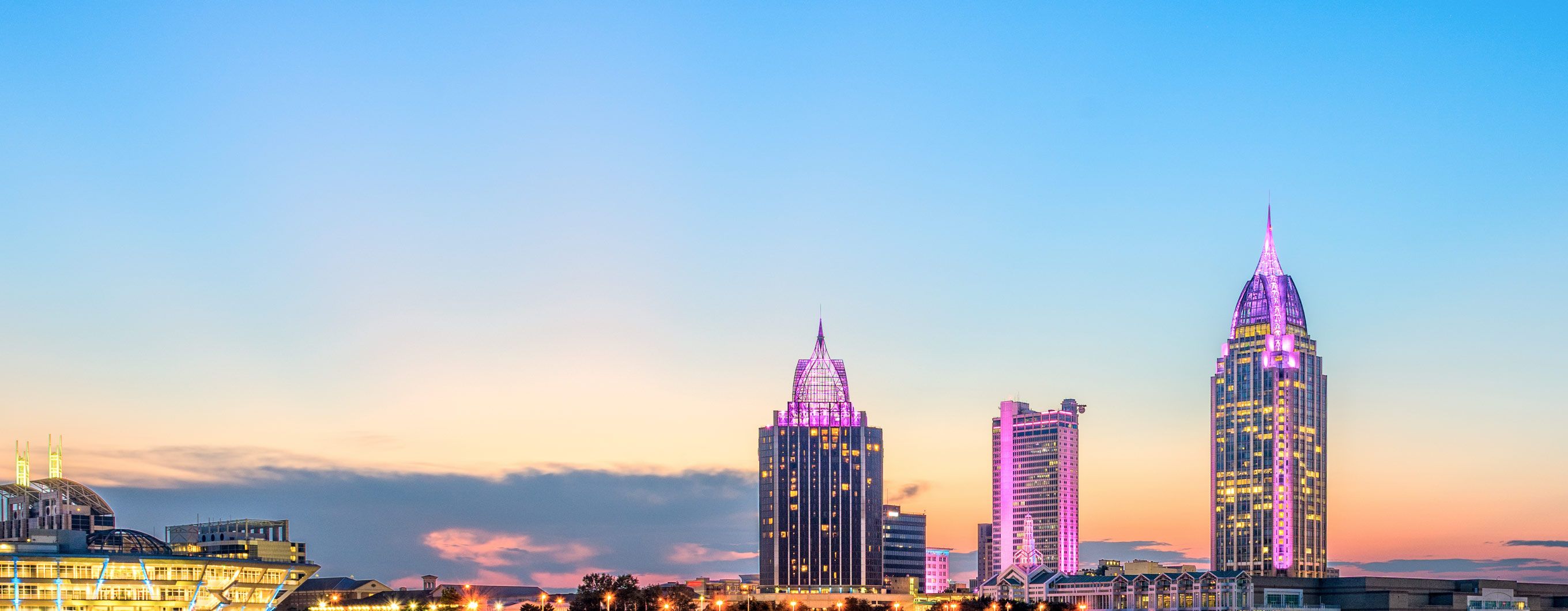 Image of three Alabama skyscrapers lit up pink with the sun setting behind them