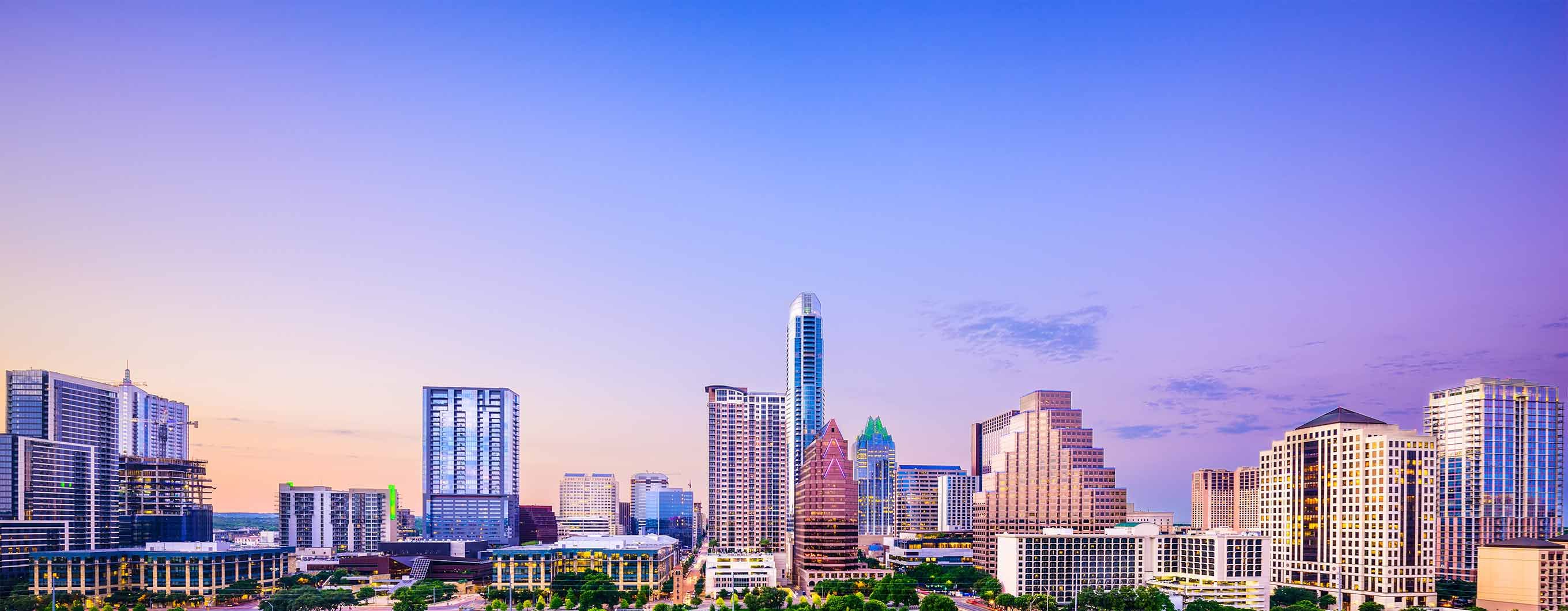 Image of the Austin city skyline with a blue and purple sky behind the buildings with a few small clouds
