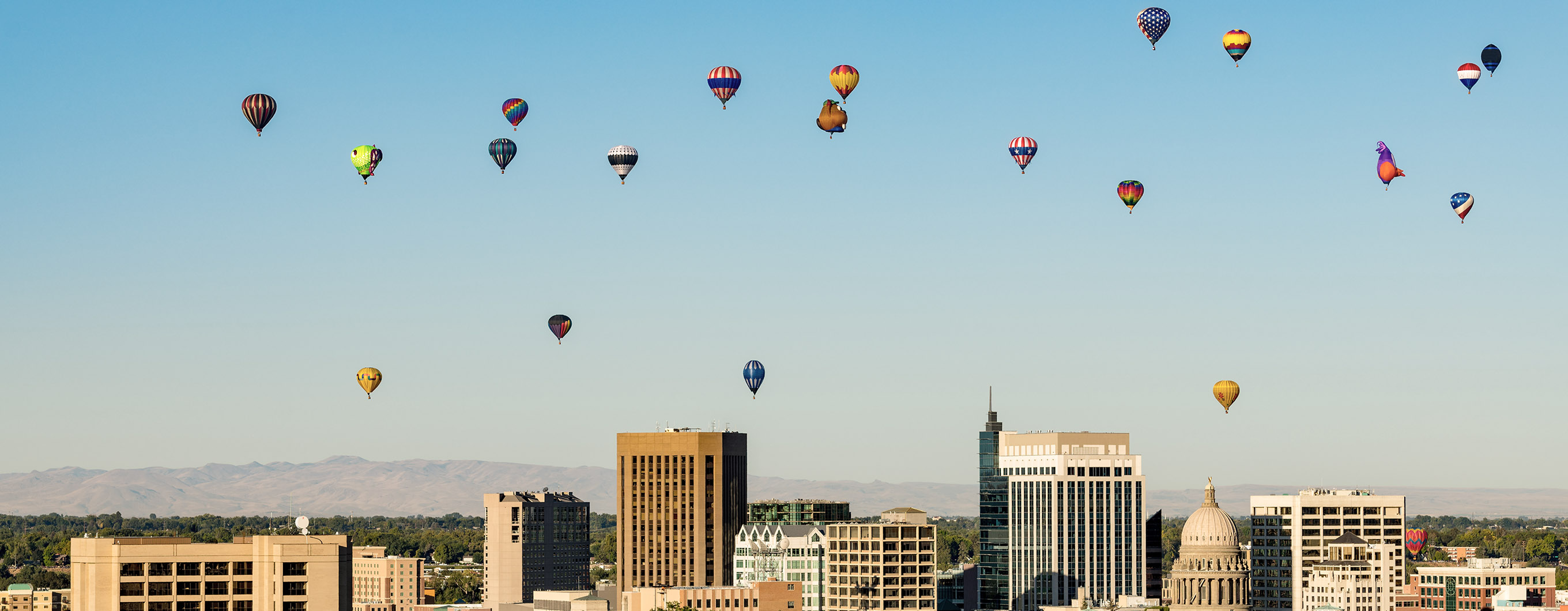 Image of the Boise skyline with hot air balloons in the partially cloudy sky.