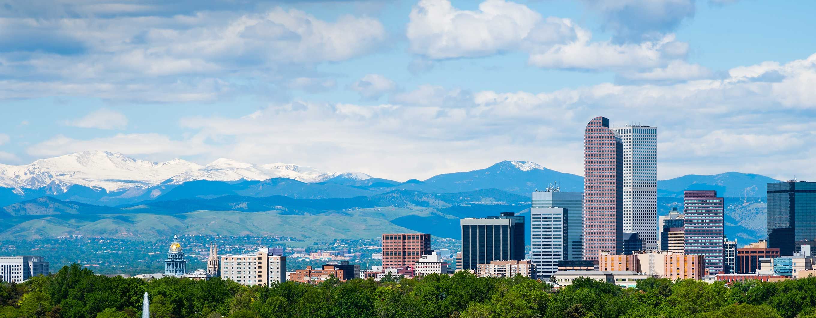 Image of the Denver skyline with mountains and a blue sky behind