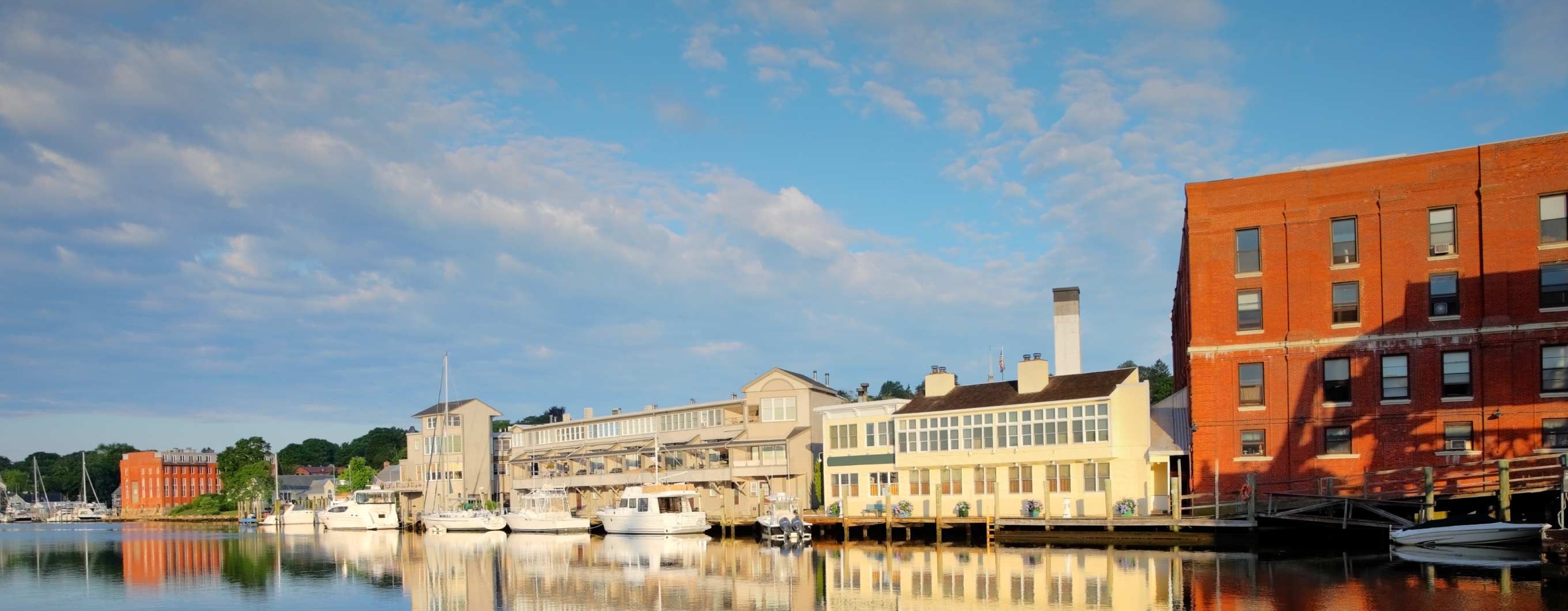 Image of several buildings in front of a body of water, with a few boats floating by wooden docks